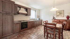 A kitchen with wooden cabinets, a granite countertop, a built-in oven, and a dining area with a wooden table and chairs. - Domus Magna by Interhome (Povoletto)