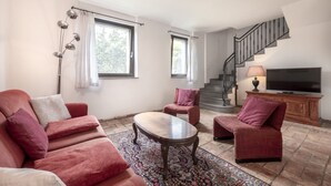 A living room with a sofa, armchairs, a coffee table, a TV, and a staircase. - Domus Magna by Interhome (Povoletto)