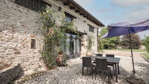 A stone building with a cobblestone patio, outdoor seating, and a large umbrella. - Domus Magna by Interhome (Povoletto)