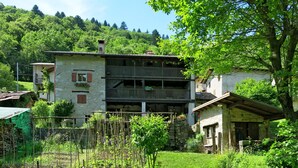 A two-story stone building with a balcony, surrounded by lush greenery and a hilly backdrop. - Casa Polava by Interhome (Valli del Natisone)