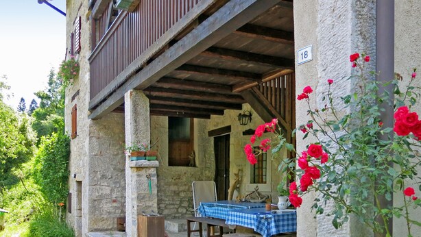 A stone building with a balcony, a table with a blue checkered tablecloth, and potted plants. - Casa Polava by Interhome (Valli del Natisone)