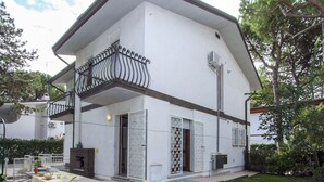Una casa de dos pisos con un balcón, un pequeño patio con mesa y sillas, y un césped bien cuidado.