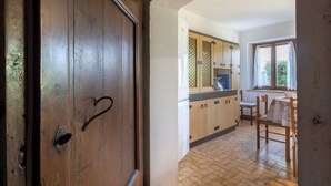 A kitchen with wooden cabinets, a window with curtains, and a dining area with a table and chairs. - Il Castelliere by Interhome (Rive d’Arcano)