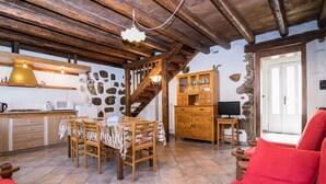 A cozy kitchen with wooden beams, a stone wall, a dining table with chairs, a wooden cabinet, and a television. - Al Rustico by Interhome (San Giovanni al Natisone)