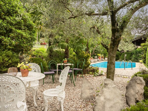 A poolside area with a pool, surrounded by greenery, stone seating, and potted plants.