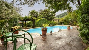 A swimming pool surrounded by lush greenery, stone flooring, and potted plants.