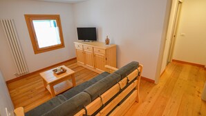 Un espacio habitable pequeño con un sofá, un televisor sobre un mueble de madera y una mesita.