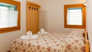 Une chambre à coucher avec un lit, deux fenêtres, une armoire en bois et un radiateur.