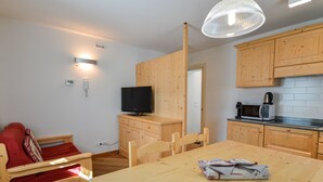 A compact living space with a kitchenette, a dining table, a TV, and a sofa.