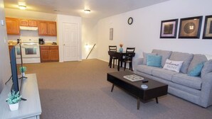 A living room with a grey sofa, a coffee table, a TV, and a kitchen in the background.