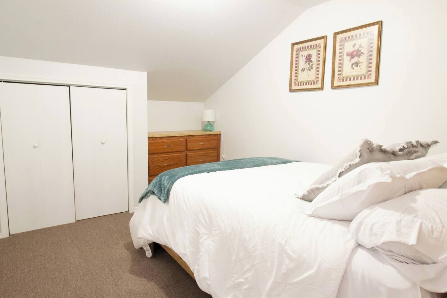 Een slaapkamer met een bed, een kastje en twee ingelijste foto's aan de muur.