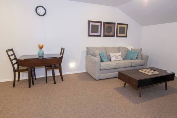 A living room with a dining table, chairs, a sofa, a coffee table, and three framed pictures on the wall.