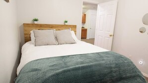 A bedroom with a bed, a wooden headboard, two pillows, a green blanket, and a white door.