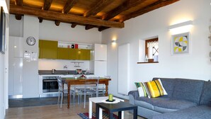 A modern living room with a grey sofa, wooden dining table, and a kitchen in the background.