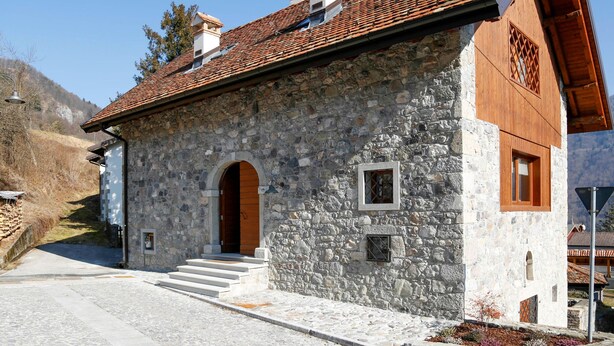 A stone building with a tiled roof, a wooden door, and a small window.