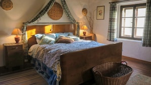 A traditional bedroom with a wooden bed, two bedside tables with lamps, a wicker basket, and a window with curtains. - Casa del Ligustro by Interhome (Strassoldo)