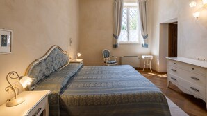 Een slaapkamer met een bed, nachtkastje, lamp, kaptafel en een raam met gordijnen.
