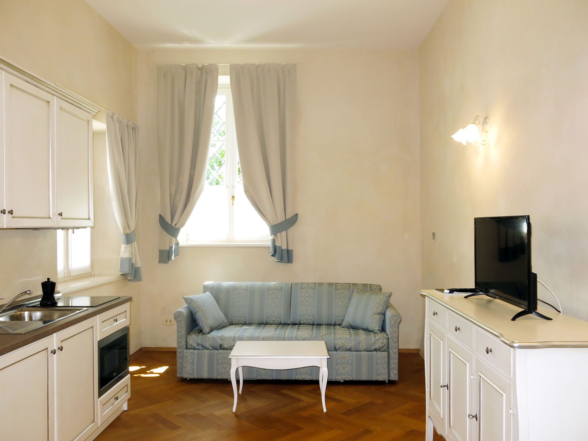 A compact living space with a kitchenette, a sofa, a television, and a small table.