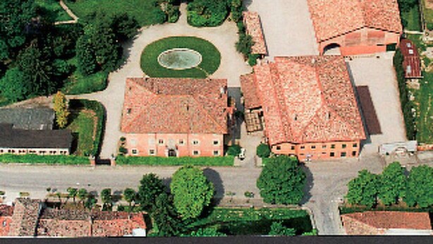 Vue aérienne d’un bâtiment historique doté d’une cour intérieure, entouré d’une végétation luxuriante et de champs.