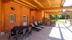 Une terrasse extérieure dotée d’un plafond en bois, d’un sol en pierre et d’un espace détente avec des chaises à rayures et une table.
