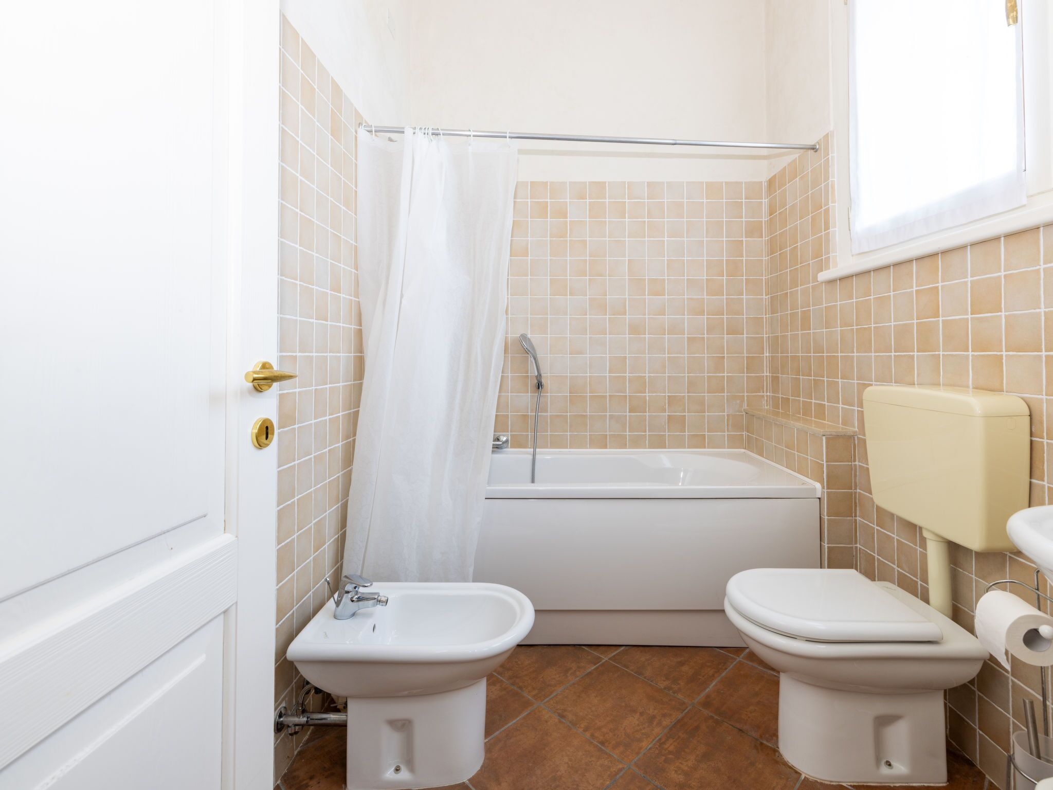 A bathroom with a bathtub, two toilets, and a bidet.