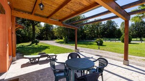 A covered outdoor seating area with stone flooring, wooden beams, and a view of a grassy path and trees. - Winery Villa Vitas Dépendance (App.1) by Interhome (Strassoldo)
