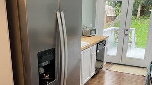 Un réfrigérateur en acier inoxydable doté d’un appareil à glaçons intégré, de meubles blancs et d’un plan de travail en bois.