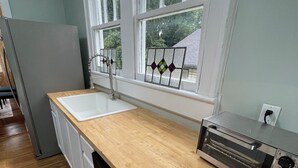 Une cuisine dotée d’un plan de travail en bois, d’un lave-vaisselle encastré, d’un four grille-pain en acier inoxydable et d’une fenêtre avec des vitraux décoratifs.