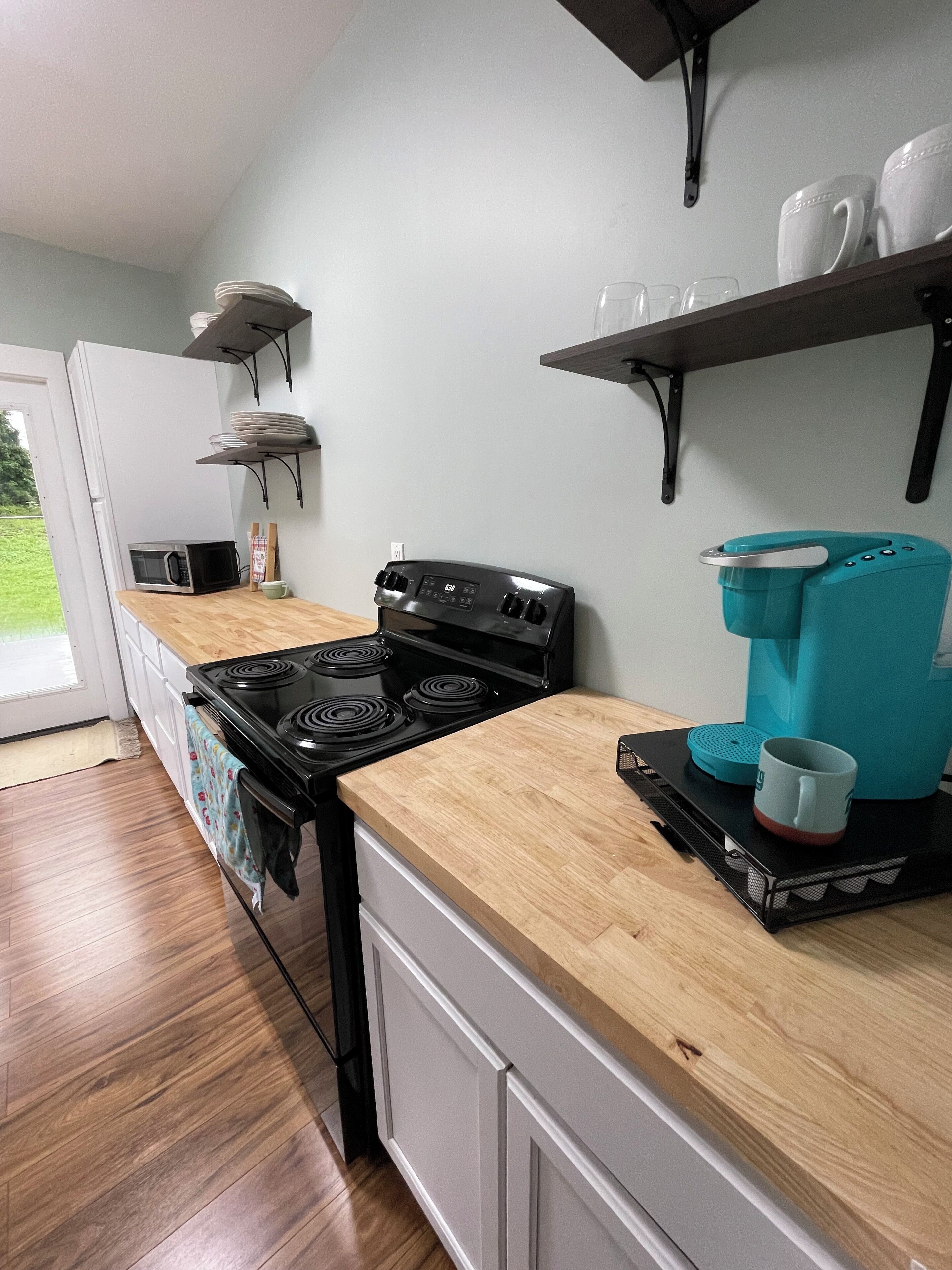 A kitchen with a black stove, wooden countertop, and a coffee maker on a tray.