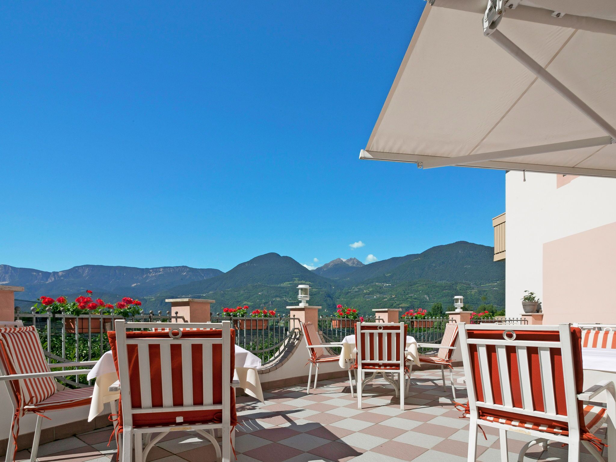 Une terrasse avec des chaises à rayures blanches et rouges, une table et un parasol blanc. La terrasse offre une vue sur un paysage montagneux.
