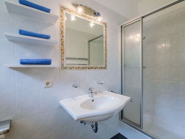 A bathroom with a white sink, a glass shower enclosure, and blue towels on shelves.