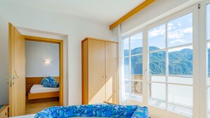 Un dormitorio con cama, armario y ventana grande con vistas a la montaña.