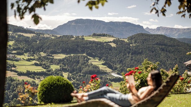 A person relaxing on a hammock overlooking a mountainous landscape with a river and greenery. - Comfort 301 by Interhome (Villandro Villanders)