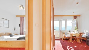 Une chambre avec un lit, une table à manger avec des chaises, une fenêtre donnant sur un beau paysage et une moquette rouge.
