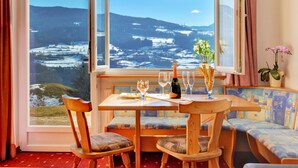 Ein Essbereich mit Tisch für vier Personen, einer Bank und Blick auf eine verschneite Landschaft durch große Fenster.