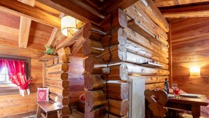L’intérieur d’un chalet en bois comprend un coin repas, une cheminée et une fenêtre ornée de rideaux rouges.