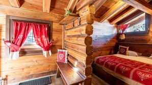 Une pièce chaleureuse dans un chalet, avec des murs en bois, un lit avec une literie rouge, un banc et une fenêtre ornée de rideaux rouges.