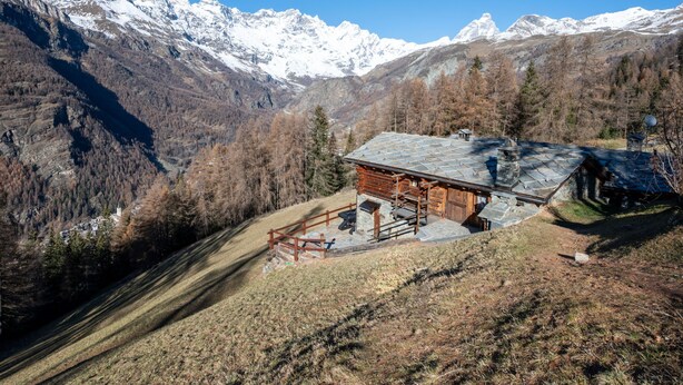 Une cabane en bois, dotée d’un toit en pente, entourée d’une forêt et de montagnes enneigées.