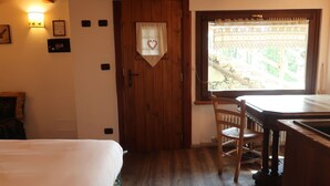 Una habitación con una cama, una puerta de madera, una ventana con vistas, una mesa y una silla.