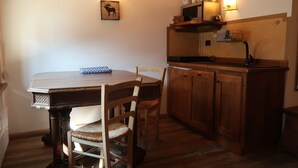 Un comedor con una mesa y sillas de madera, una pequeña cocina con microondas y fregadero, y un aplique de pared con siluetas de animales.