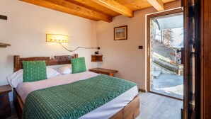 Ein Schlafzimmer aus Holz mit einem Bett, Nachttischen, einer Wandlampe und einer Tür zu einem Außenbereich.