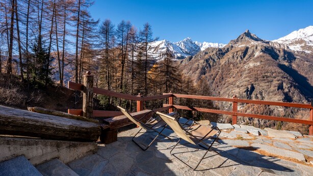 Eine Steintreppe führt zu einer Aussichtsplattform mit Holzwertung, mit Blick auf eine Berglandschaft mit schneebedeckten Gipfeln.