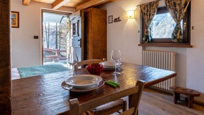 Ein Holztisch mit Tellern, Gläsern und Besteck. Ein Fenster mit Vorhängen ist sichtbar, und eine Heizung befindet sich an der Wand.