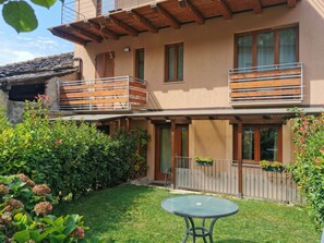 A two-story building with a balcony, a small garden, and a round table.