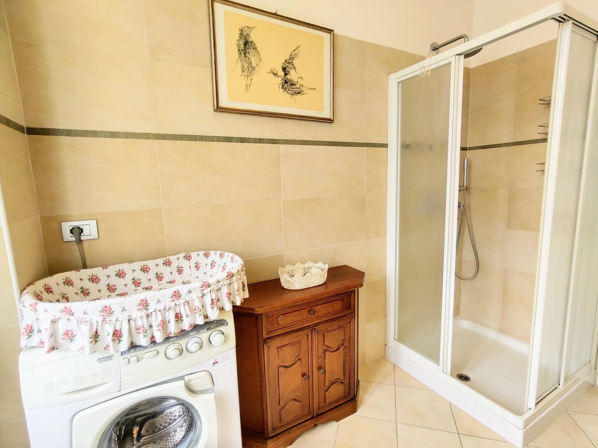 A bathroom with a washing machine, wooden cabinet, and a glass shower enclosure.