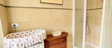 A bathroom with a washing machine, wooden cabinet, and a glass shower enclosure.