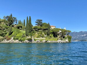 Un paysage côtier avec une colline où se trouvent des jardins bien entretenus et un bâtiment surmonté d’un toit rouge.