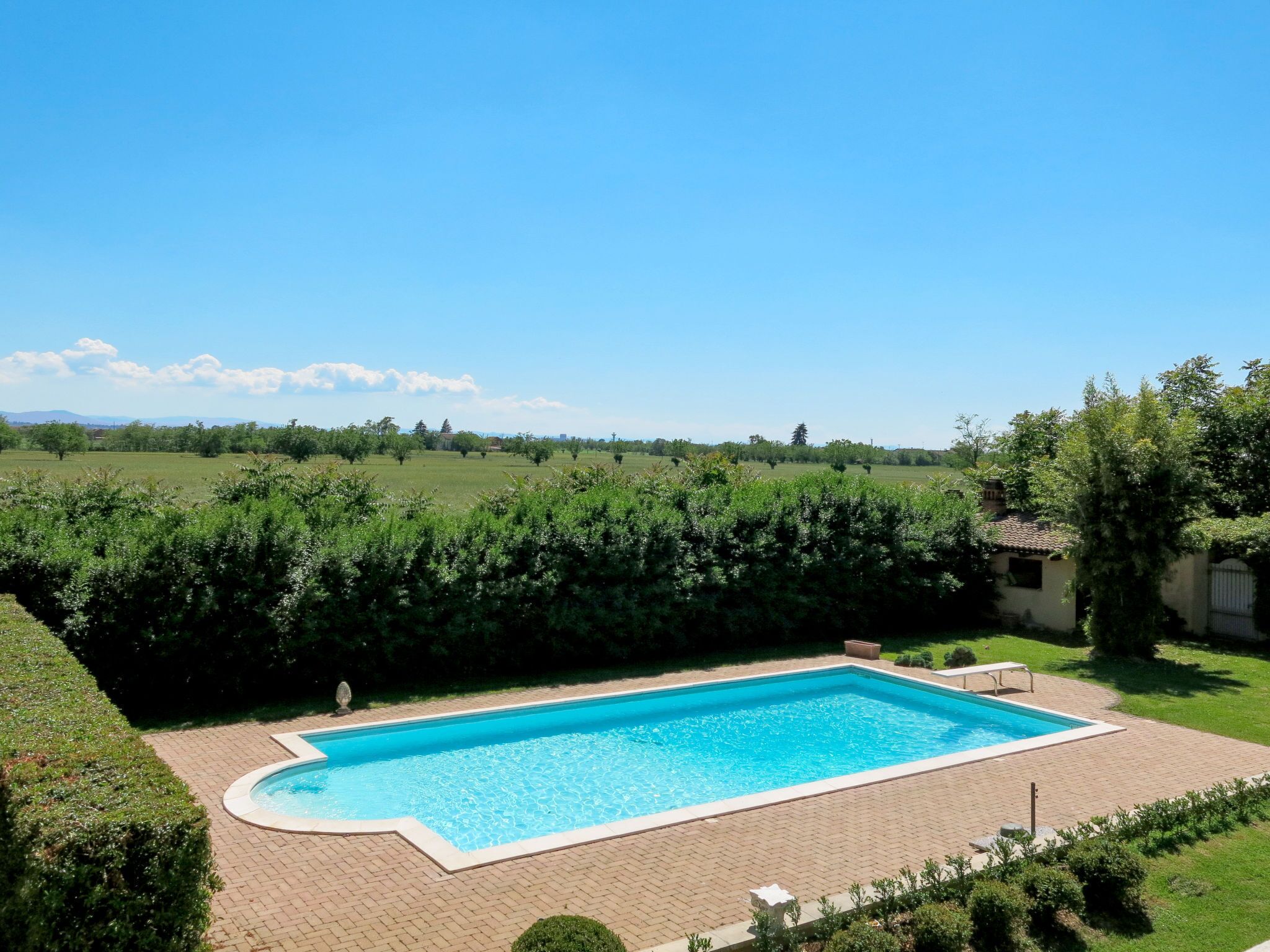 A rectangular swimming pool with a tiled deck, surrounded by well-maintained hedges and grass.