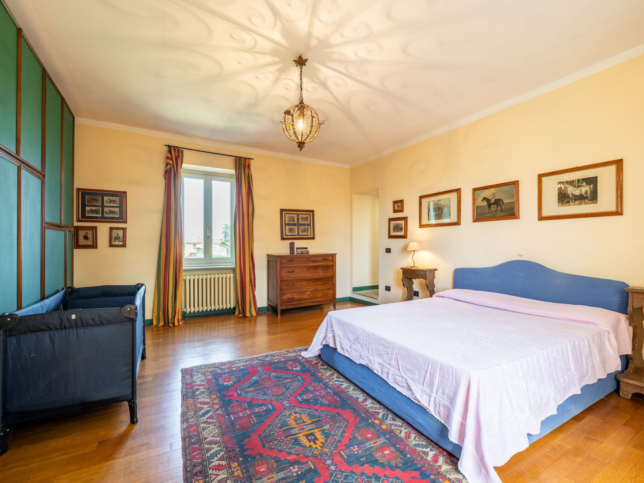 Ein Schlafzimmer mit einem großen Bett, einem Schminktisch, einem Heizkörper und einem Fenster mit Vorhängen.