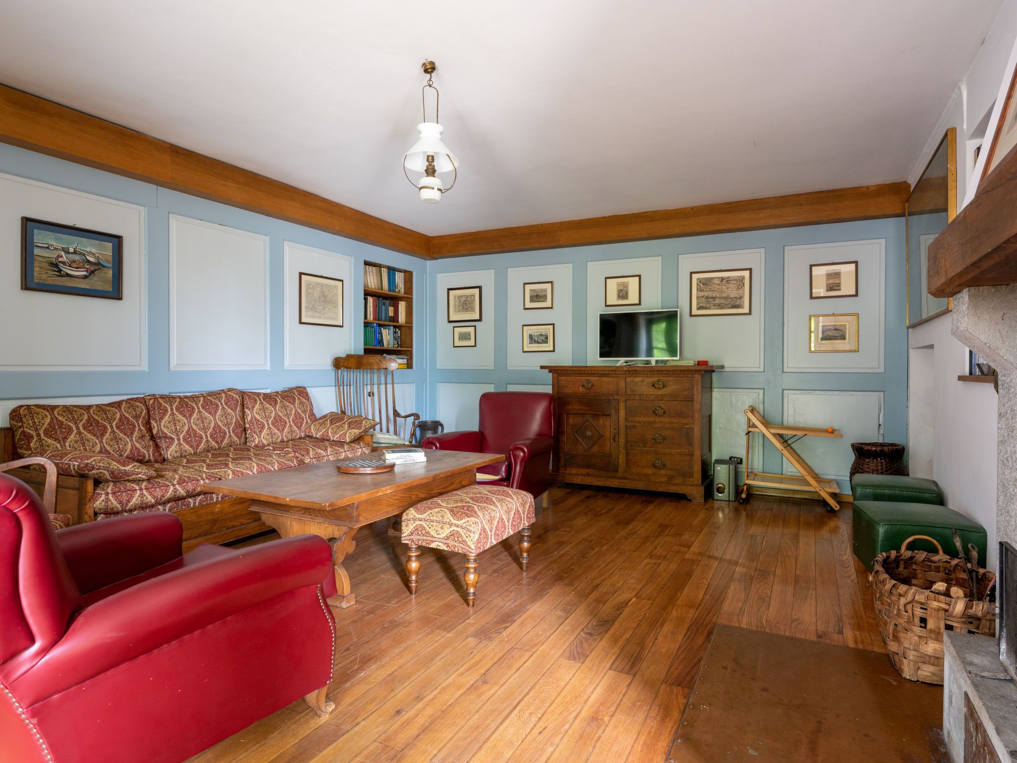 A room with a wooden floor, a red sofa, a wooden coffee table, a red armchair, a wooden cabinet, and a television on a stand.